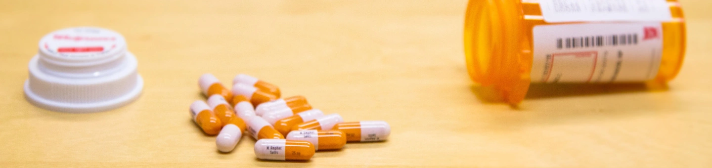 Open Adderall bottle on its side with pile of Adderall pills