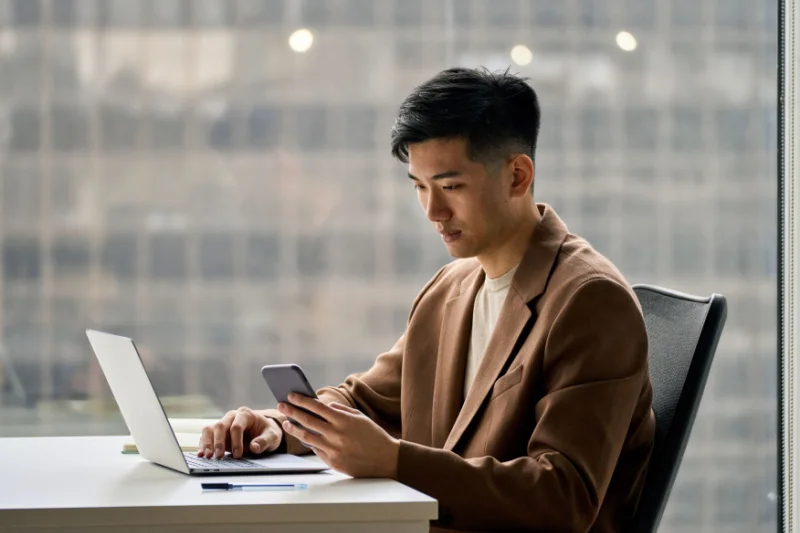 Young man conducts research on his phone and computer on different IOPs