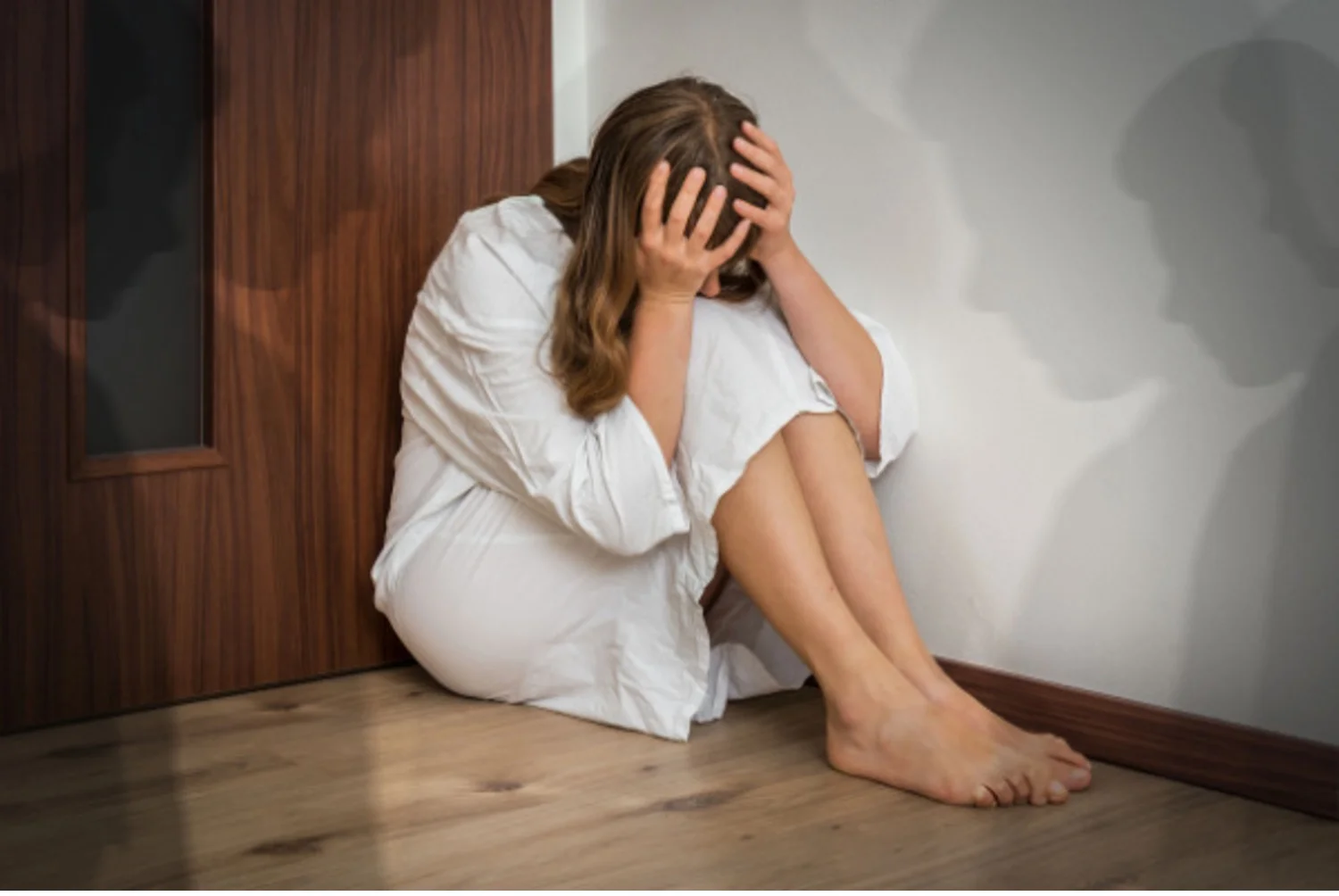 Hallucinating, scared woman sits in a corner with shadow people around her