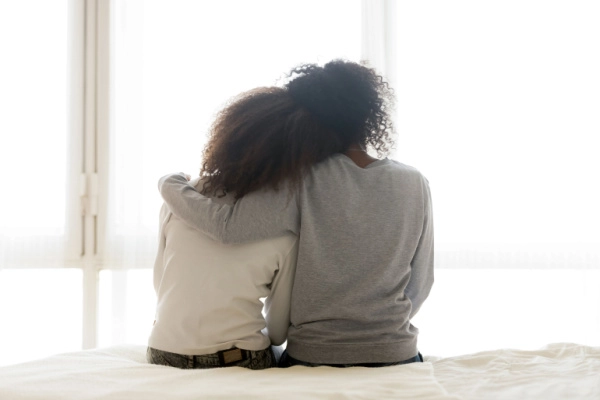 Mom puts reassuring arm around her daughter's shoulders as they look out the window