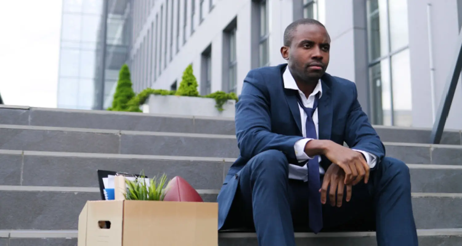 Sad businessman who’s just been fired sits on steps with a box of his office supplies