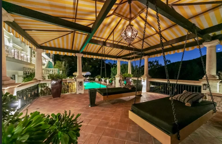 Outdoor covered terrace adjacent to swimming pool with beds hung from the ceiling