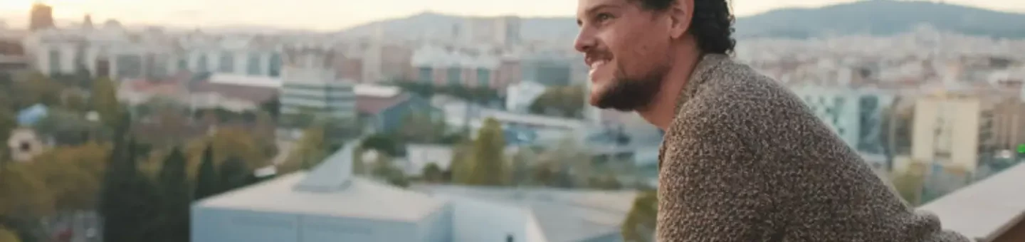 Happy, confident man leans on balcony railing overlooking city below