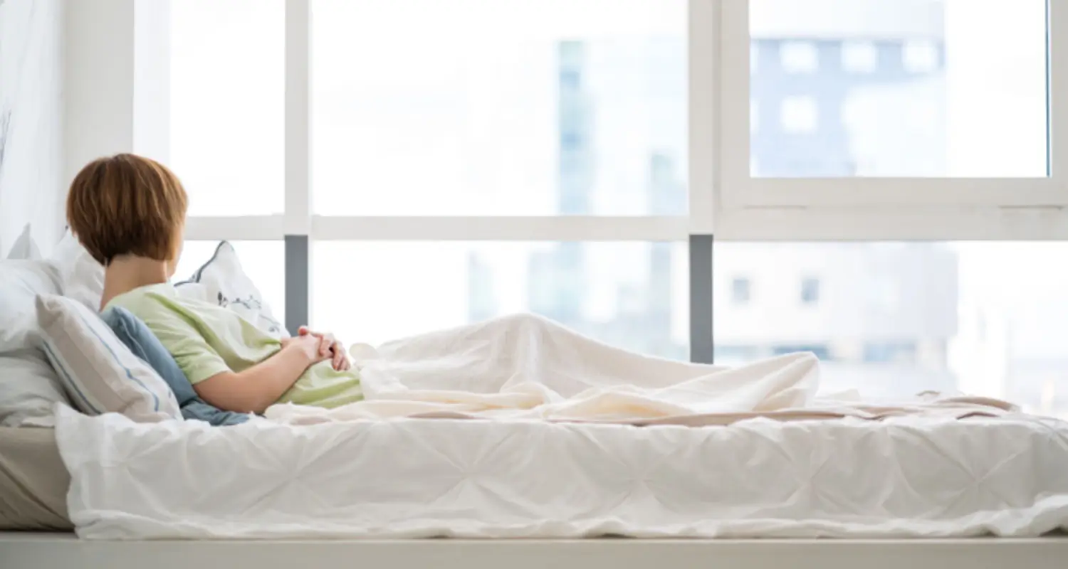 Woman in inpatient heroin rehab sits in bed and looks out the window