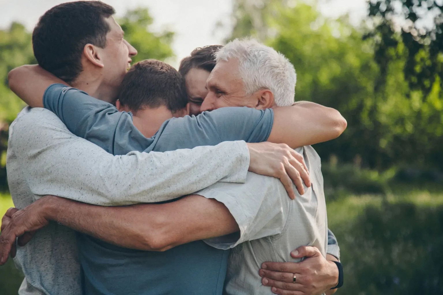 Group of men in addiction recovery hug each other in an emotional embrace