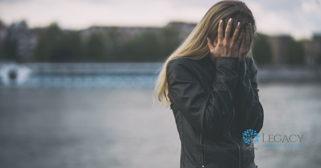 A woman in a paved lot, covering her face with her hands.